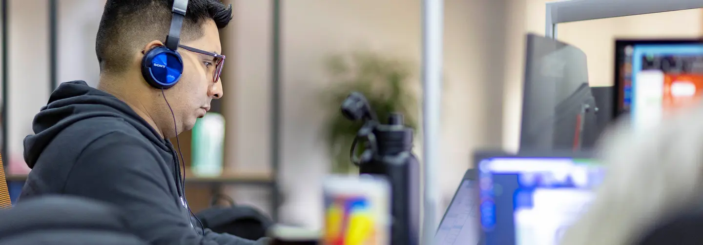 Desarrollador de Infosgroup con audífonos trabajando en computadora en oficina tecnológica